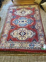 Full view of the rectangular area rug spread out on a wood floor, showing its geometric medallion pattern in red, cream, blue, and navy hues.