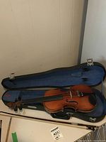 Violin placed inside an open hard case with blue interior lining and a bow resting in the case.