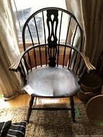 Full front view of the black wooden Windsor style captains chair in front of a window, showing curved armrests and spindle backrest.