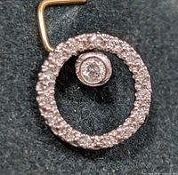 Close-up of a circular pendant with pave diamonds around the outer circle and a bezel set central diamond on a dark background.