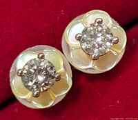 Close-up image of the front view of the pair of earrings showing round diamonds centered over mother of pearl floral shapes on a red background.