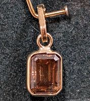 Front view of pendant showing bezel set emerald cut diamond in 10KT yellow gold.
