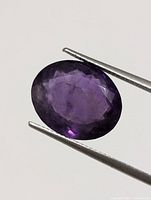 Close-up image of an oval faceted purple amethyst held in tweezers showing color and clarity.