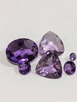 Six faceted amethyst gemstones of varying sizes and shapes arranged on a white background.