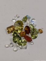 Loose assorted genuine gemstones in various colors and cuts on a white surface