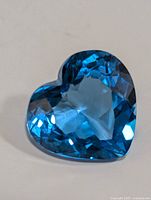 Close-up photo of the heart-shaped blue topaz gemstone showing its vibrant blue color and faceted surface.