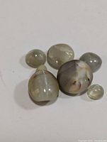 Six genuine cat's eye cabochon gemstones shown on white background, displaying translucent body and chatoyancy.