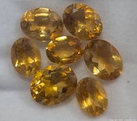 Seven oval faceted citrine gemstones displayed on a white background, showing their golden yellow color and clarity.