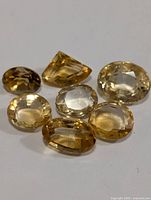 Seven faceted citrine gemstones of varying shapes and sizes arranged on a white surface to show color and cut detail.