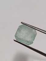 Close-up of the Colombian emerald gemstone held by tweezers showing the cut and clarity.