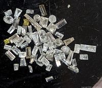 Top-down view of loose genuine diamonds on a black surface showing multiple shapes and few colored stones