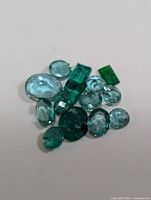 Close-up of mixed oval and rectangular emerald and aquamarine gemstones on white background.