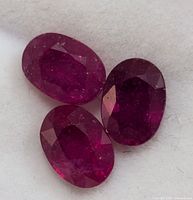 Four oval cut, deep red, genuine enhanced rubies displayed on a white background.