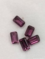 Five faceted rectangular cut garnet gemstones against white background
