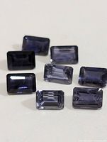 Eight rectangular faceted iolite gemstones arranged on a white surface showing color and cut details.