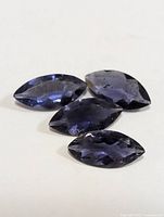 Four marquise cut violet-blue iolite gemstones placed on white background, showing faceted surfaces and natural inclusions from multiple angles.