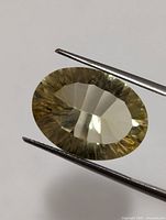 Oval faceted lemon quartz gemstone held with tweezers showing the flat table and faceted pavilion, light yellow color and transparency