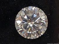 Close-up image of loose round brilliant cut clear gemstone on black velvet background showing facets and fire.