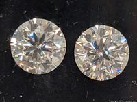 Close-up of two round cut sparkling moissanite stones on black background showing facet detail.