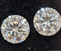 Close-up of two round brilliant cut moissanite stones on black background showing facets and brilliance.