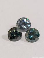 Three loose faceted round cut moissanite stones on a white background.