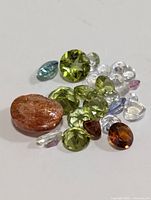 Photo showing a collection of various loose genuine gemstones including green, blue, brown, orange, and clear stones in different cuts.
