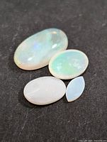 Four loose genuine opal gemstones on black background showing color play and shapes