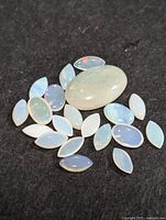 Clear photo of a group of 22 genuine opal gemstones placed on a dark surface showing their opalescent colors and shapes.