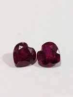 Two heart-shaped rubies placed on a white surface, showing color and cut details.
