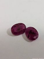 Two oval-shaped faceted rubies with natural inclusions shown on white background.