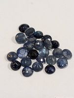 Multiple loose round faceted sapphire stones on white background clustered together.