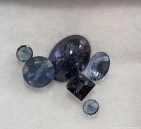 Close-up of six loose sapphire gemstones on a white background showing various cuts and blue shades.