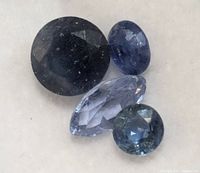 Four loose sapphires of different cuts and shades, laid on a neutral background.