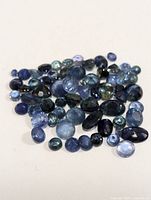 Multiple loose sapphire gemstones of various sizes and blue shades, photographed on neutral background.