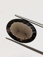 Oval cut genuine Smokey Quartz gemstone approximately 10 carats held by tweezers
