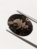 Oval cut smokey quartz gemstone held by tweezers showing the brown translucent facets and internal reflections.