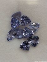 Close-up views of multiple faceted tanzanite stones in triangular cuts with violet-blue color on a white background.