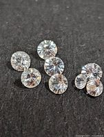 Close-up photo of the loose white sapphire stones arranged on black fabric, showing their round faceted cuts and clear color.