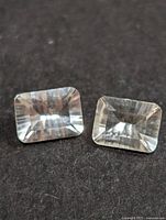 Two clear rectangular white topaz gemstones viewed from above on a dark background.
