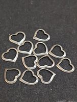 Photo showing all 12 silver-tone floating heart-shaped metal charms arranged loosely on black fabric.