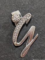 Close-up photo of silver letter "C" shaped pendant decorated with small cubic zirconia stones on the curve and a larger round cubic zirconia set in a flower-shaped setting on the top left.