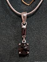 Close-up of garnet pendant on silver snake chain showing round faceted garnet in prong setting with rectangular garnet above.
