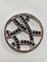 Front view of round silver pendant with multiple curved intersecting bands set with black gemstones.