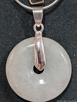 Close-up of circular pale green translucent jadeite pendant with silver bail on black background.