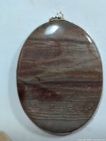 Top view of large oval genuine gemstone pendant with silver setting showing natural striations and polished surface.