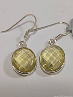 Front view of pair of silver earrings, each with an oval faceted lemon quartz in bezel setting and hook backs.