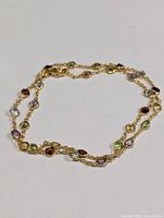 Gold-tone silver chain necklace with round bezel-set faceted gemstones in multiple colors displayed laid down