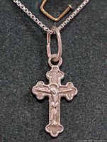 Close-up front view of silver crucifix pendant on silver chain necklace on black background.