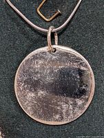 Photo showing front side of the round silver pendant attached to a silver snake chain necklace, with surface scratches visible.