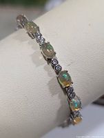 Silver bracelet with alternating oval opal cabochons and round cubic zirconia stones displayed on white bracelet stand.
